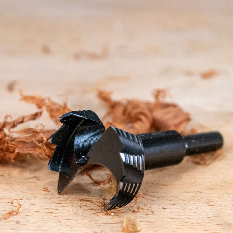 Black wood drill bit on a wooden surface with sawdust