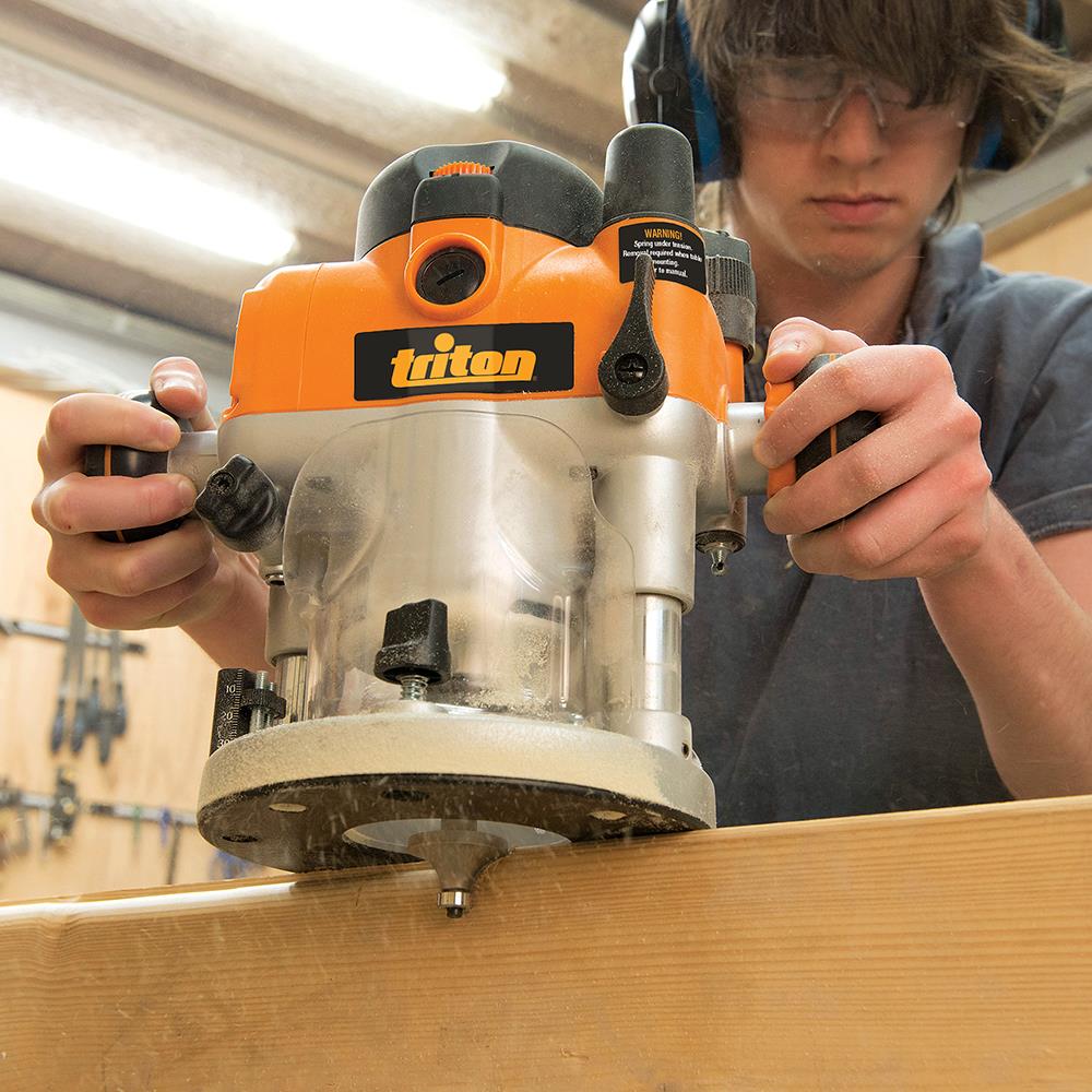 Woodworker using a Triton router on a wooden board in a workshop