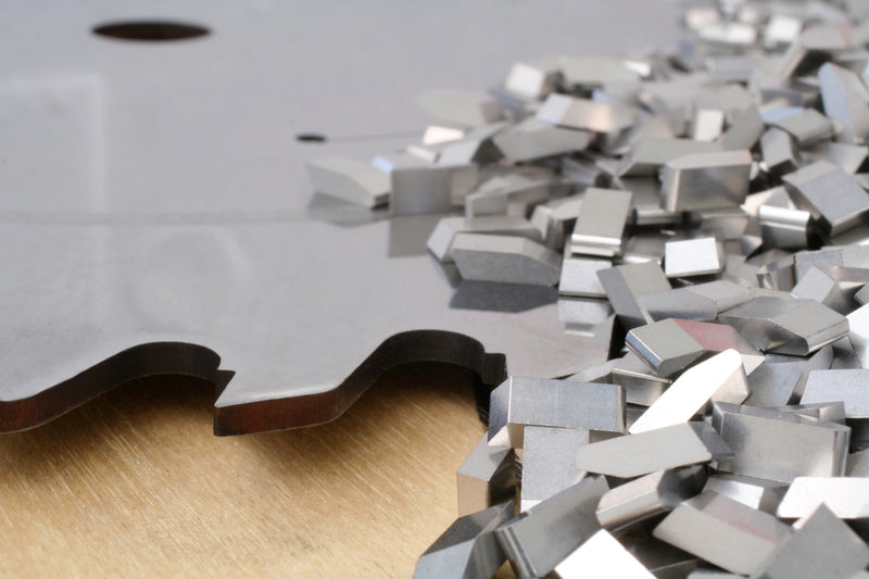 Metallic carbide saw blade tips on a wooden surface with a white background