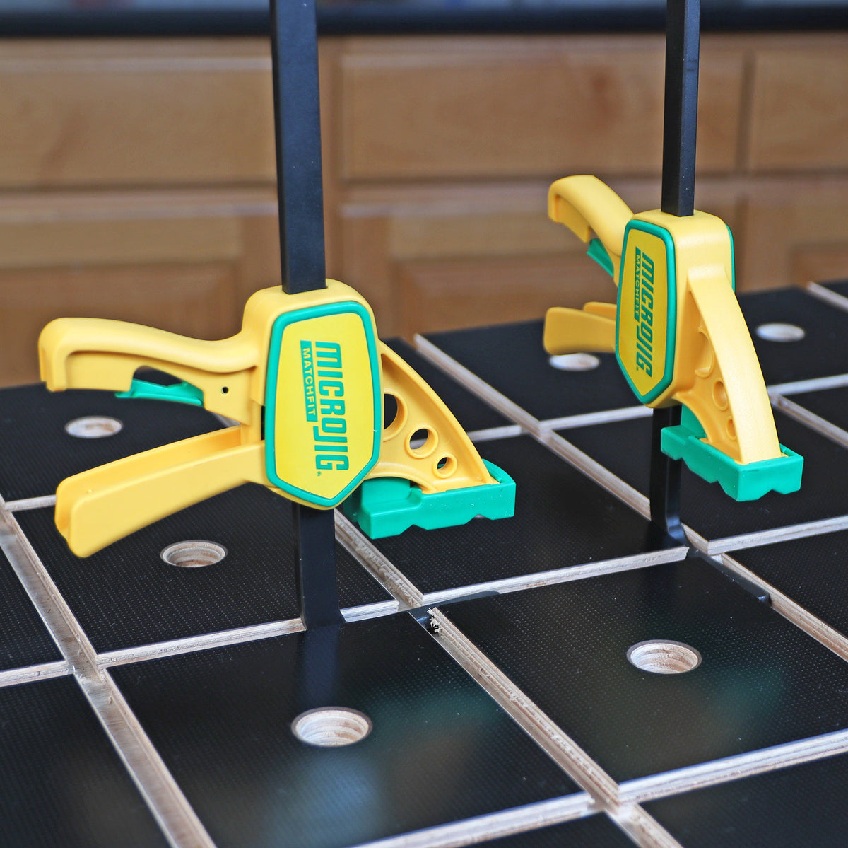 Yellow MicroJig MatchFit woodworking clamps on a slotted workbench in a workshop setting