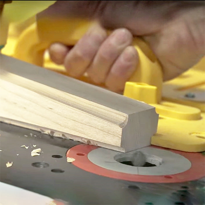 Close-up of a woodworker guiding a molding profile over a router table with safety push block