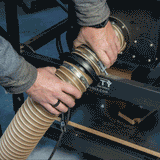 Hands connecting dust collection hose with magnetic coupling on woodworking machine
