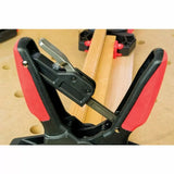 Close-up of quick-release woodworking clamp holding wooden boards on a workbench