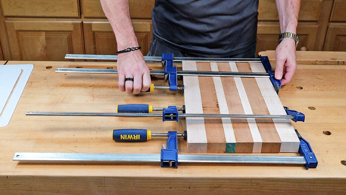 Woodworker clamping a striped wood panel with bar clamps on a workbench