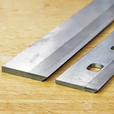 Close-up of two steel planer knives on a wooden surface, woodworking tool blades