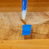 Applying wood glue to a crack in a wooden board with blue painter's tape for woodworking repair