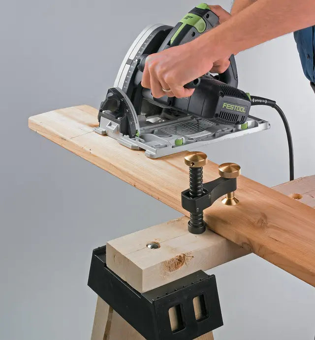 Woodworker using a Festool circular saw to cut lumber, secured with a brass clamp on a workbench.