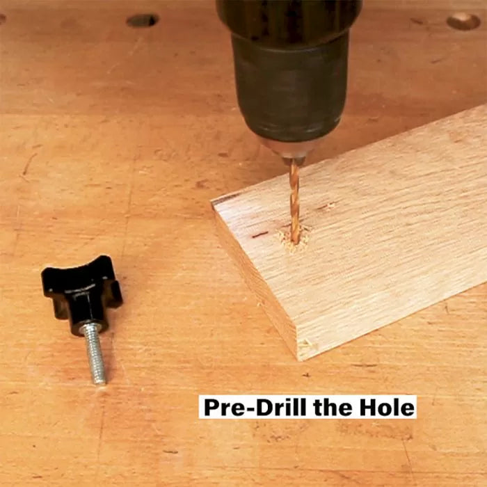 Pre-drilling a hole in a wooden board with a power drill on a workbench, woodworking hardware nearby.