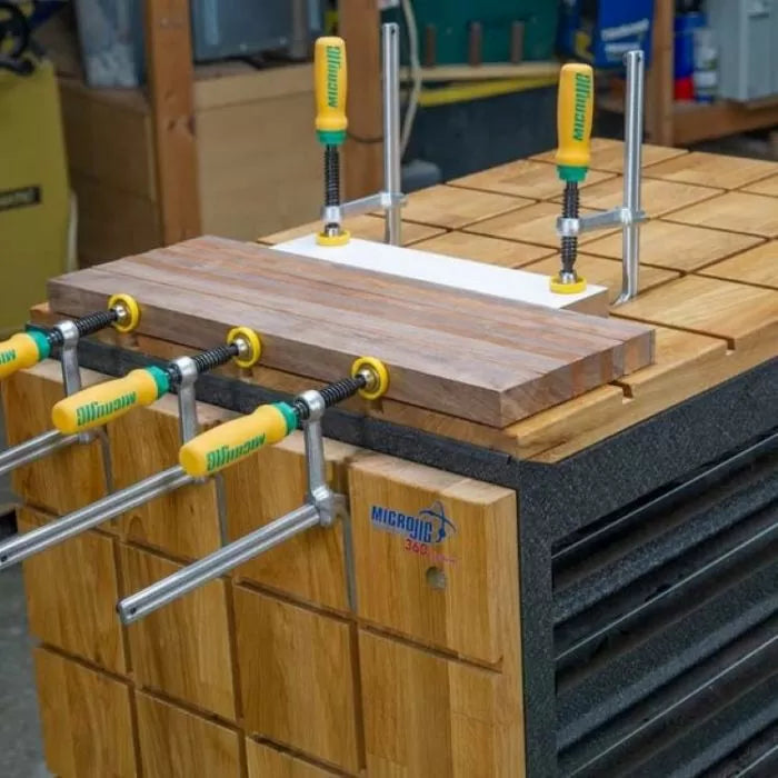 Woodworking jig system in use with multiple clamps holding a wooden board on workbench