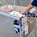 Woodworker using a domino joiner with a jig system on a workbench, wood clamps visible.