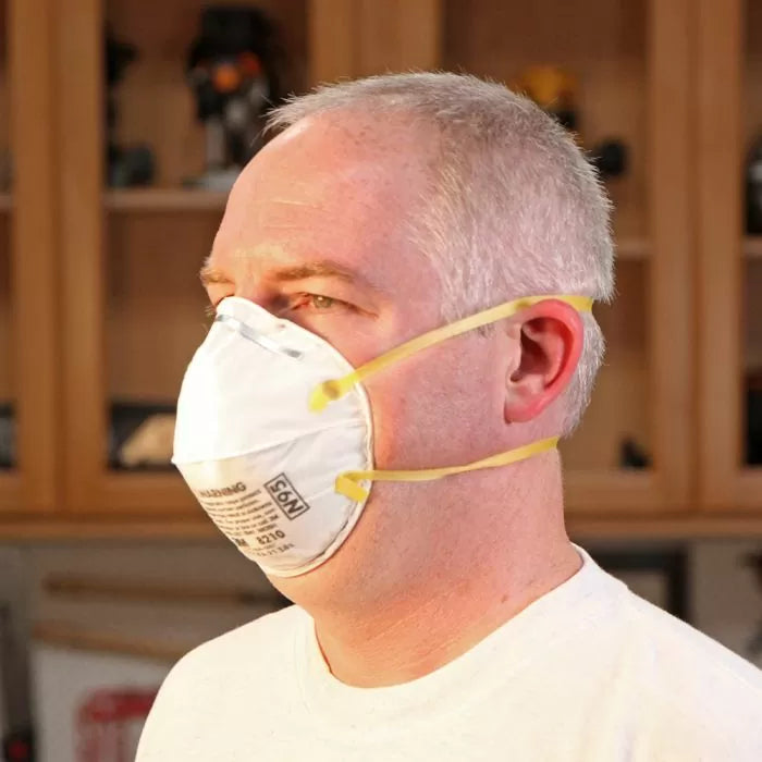 Man wearing N95 dust mask respirator with yellow straps in woodworking shop