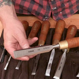 Hand holding woodworking chisel with wood handle, chisel set displayed in tool roll
