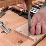 Woodworker using chisel to cut dovetail joint on hardwood at a woodworking bench
