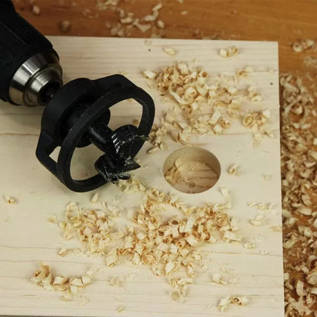 Drill with stop collar attachment and wood shavings on a drilled wooden board