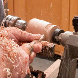 Woodworker using turning tool on a lathe with wood shavings flying in workshop