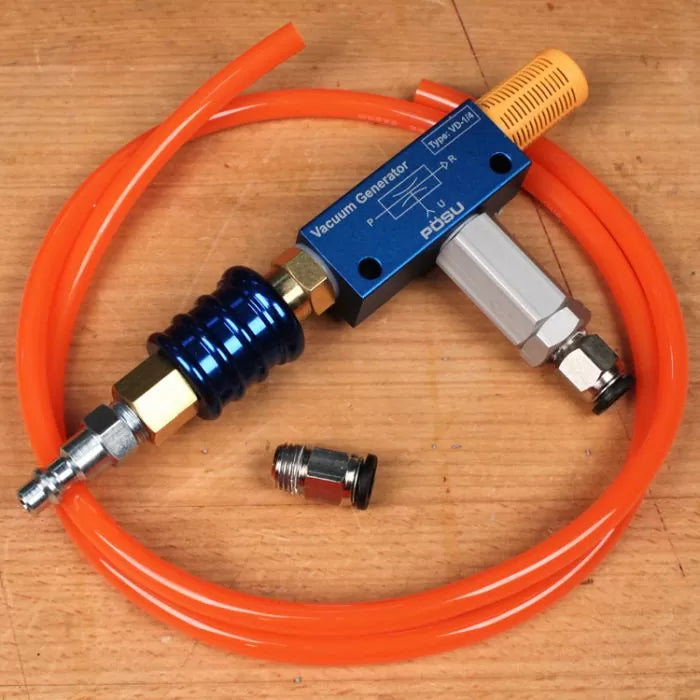 Vacuum generator kit with orange hose and fittings on a wooden surface, woodworking tool accessory.