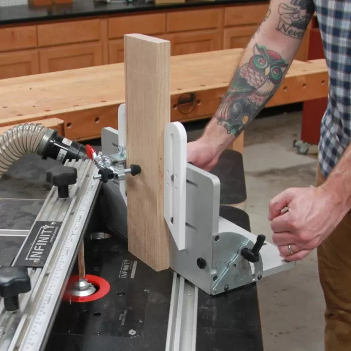Person adjusting router table fence with dust collection and vertical wood piece in workshop